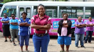 Women bus drivers standing in formation smiling in front of the Meri Safe Bus in Port Moresby, Papua New Guinea celebrating their part in a gender equality and social inclusion campaign for the 20 days of human rights activism in 2018, supported by Australia through the Abt-managed Church Partnership Program.